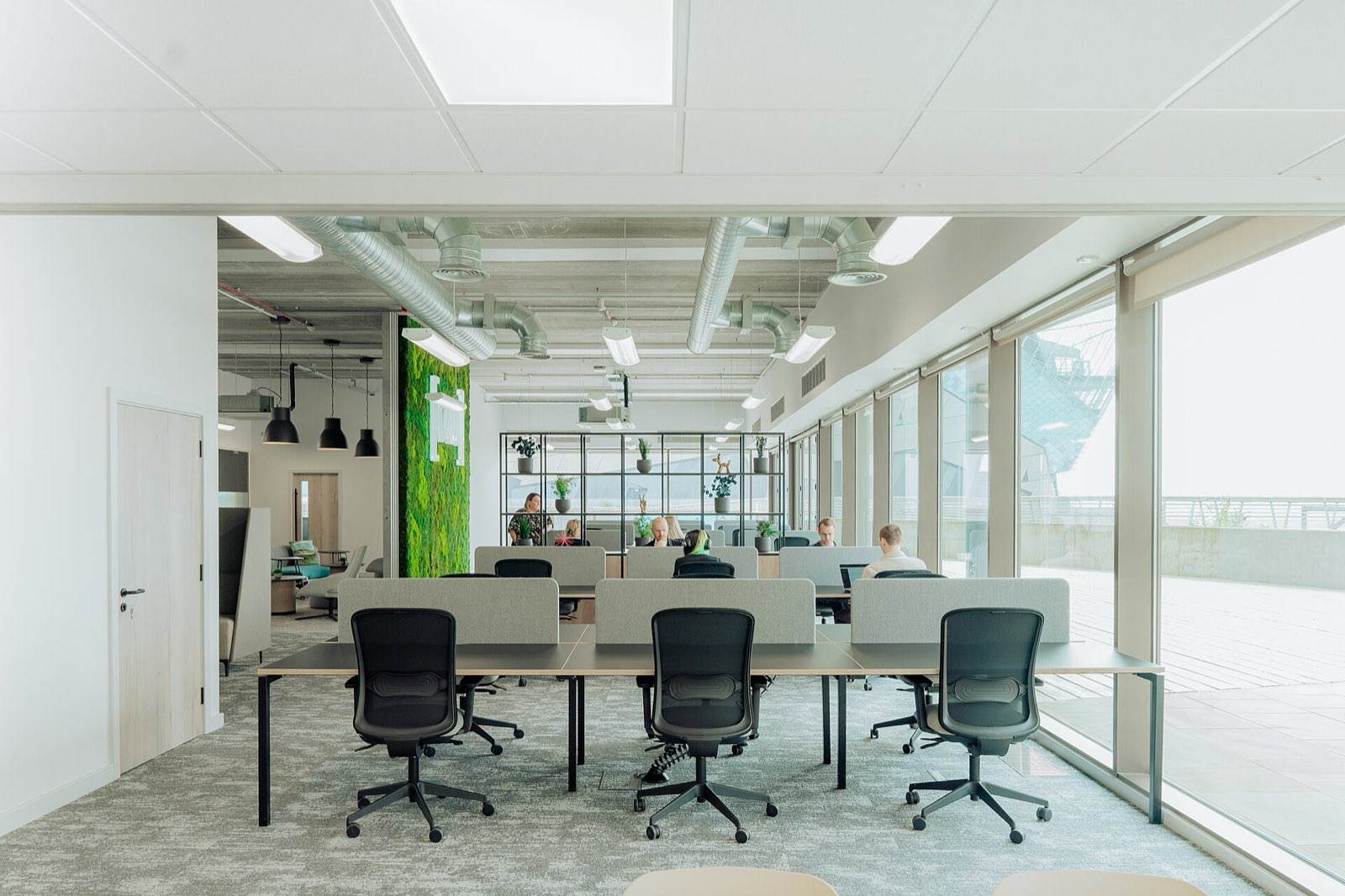 A light-filled modern office interior with long meeting tables and floor-to-ceiling windows.