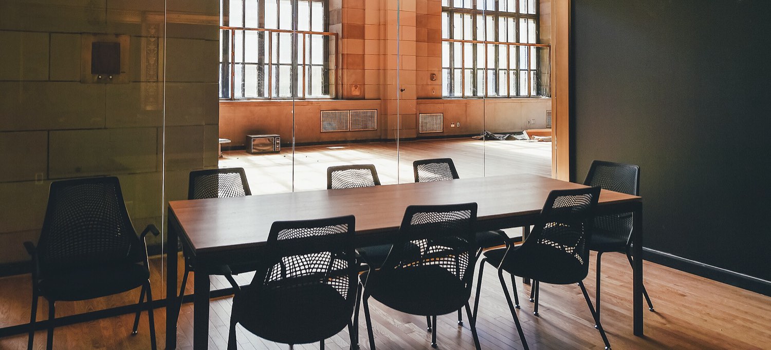 An empty boardroom with a long polished table and high-backed leather chairs.